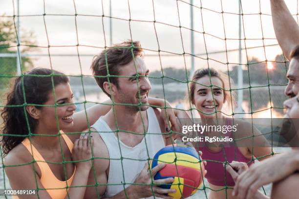 friends standing behind volleyball net - beach volleyball team stock pictures, royalty-free photos & images