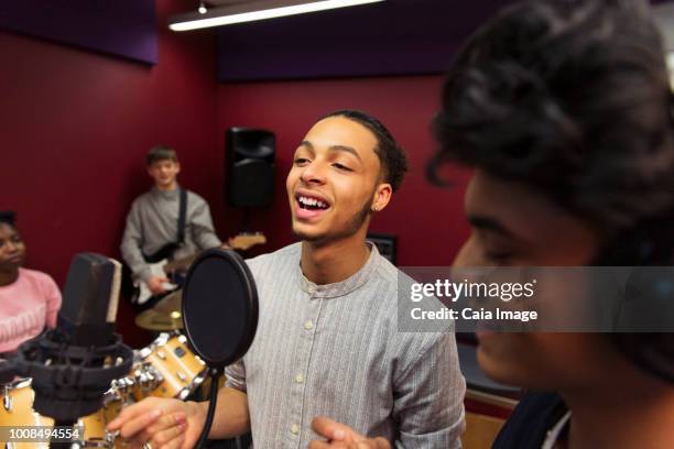 Teenage musicians recording music, singing in sound booth