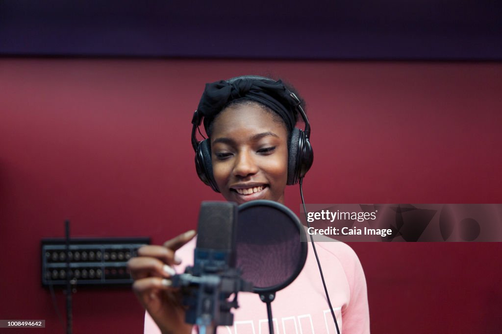 Smiling teenage girl musician recording music, singing in sound booth