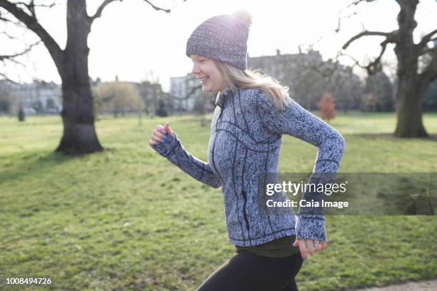 smiling female runner running in sunny park - jogging winter stock pictures, royalty-free photos & images