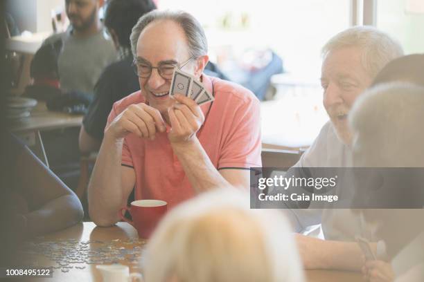 happy senior friends playing games at table in community center - senior men playing cards stock pictures, royalty-free photos & images