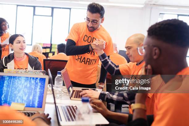 hackers handshaking, celebrating and coding for charity at hackathon - hackathon stock pictures, royalty-free photos & images