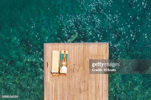 beautiful woman sunbathing alone on a wooden pier in sea aerial photo - beach bag overhead stock pictures, royalty-free photos & images