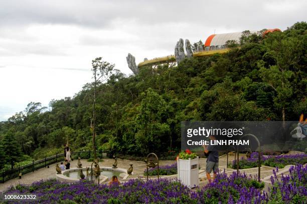 In this photograph taken on July 31 the 150-meter long Cau Vang "Golden Bridge" is seen past visitors in the Ba Na Hills near Danang. - Nestled in...