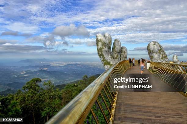 In this photograph taken on July 31 visitors walk along the 150-meter long Cau Vang "Golden Bridge" in the Ba Na Hills near Danang. - Nestled in the...