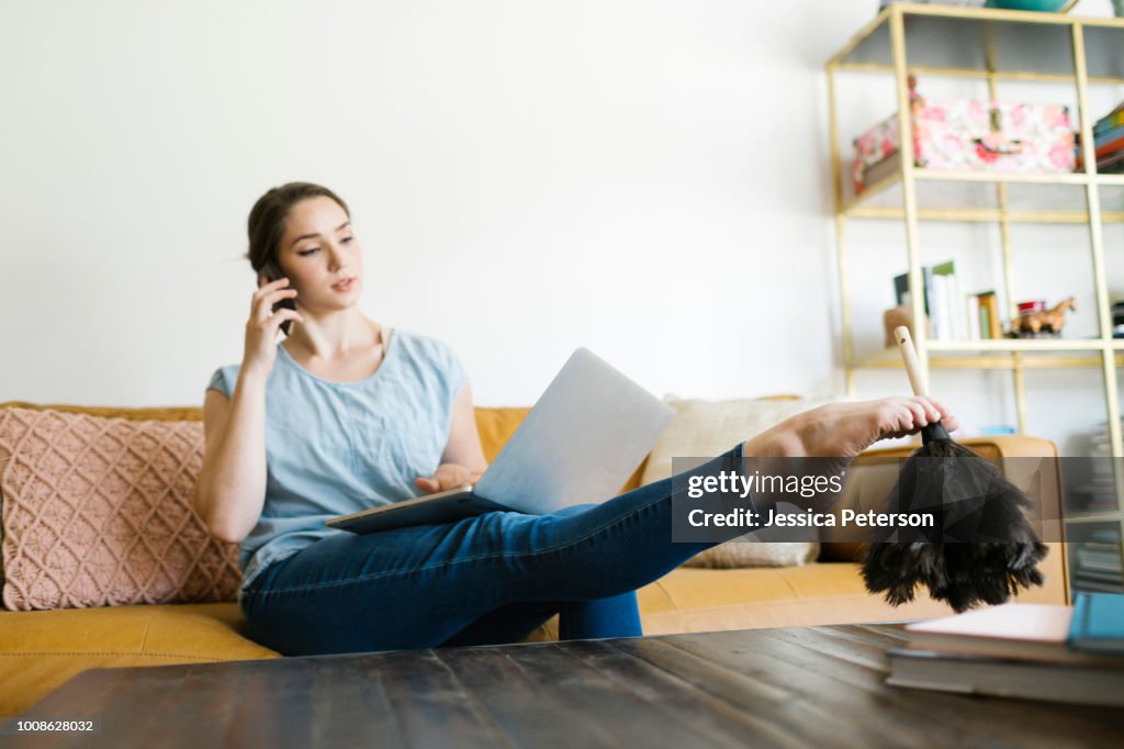 Woman using laptop and smart phone while dusting with foot