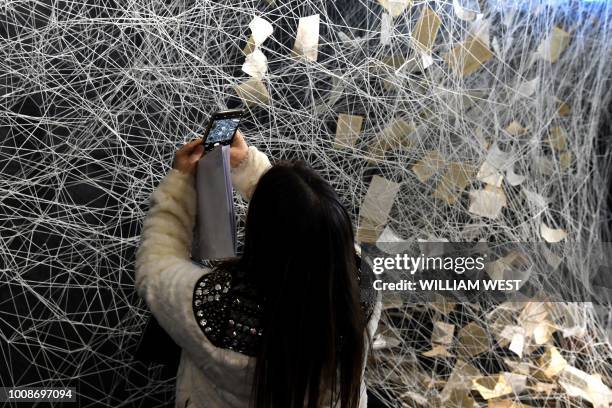 Woman takes a photo of an installation by Japanese artist Chiharu Shiota titled 'The Crossing', which features white yarn and 175 books, at a preview...