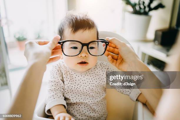 mother's hand putting on oversized glasses onto baby girl - miope and humor fotografías e imágenes de stock