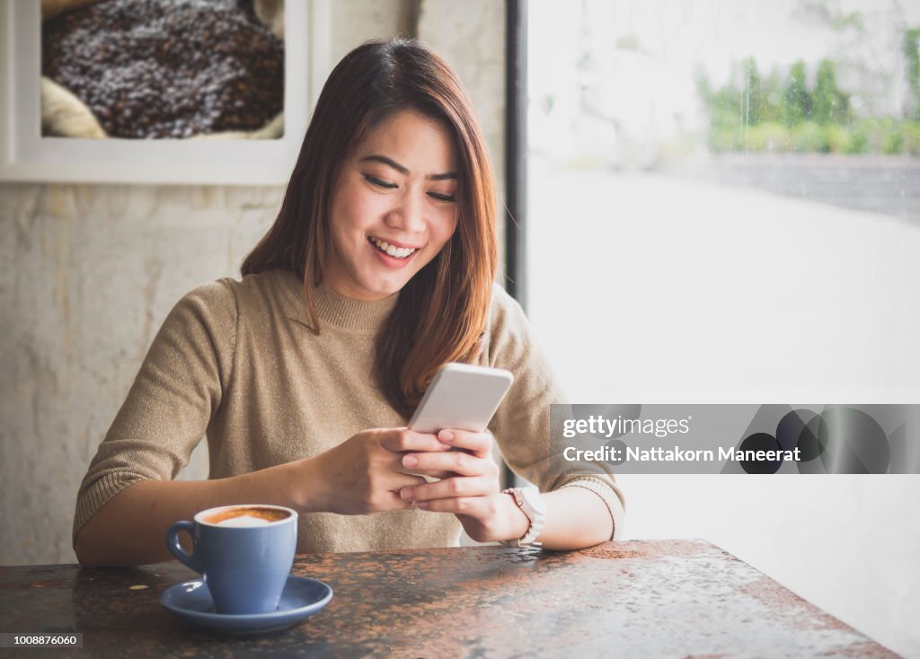年輕的亞洲美女使用智慧手機進行商務、網上購物、轉帳、金融、網上理財。在咖啡館裡模糊的背景。