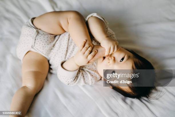 lovely baby girl lying on bed and sucks on her toes - sucking fotografías e imágenes de stock