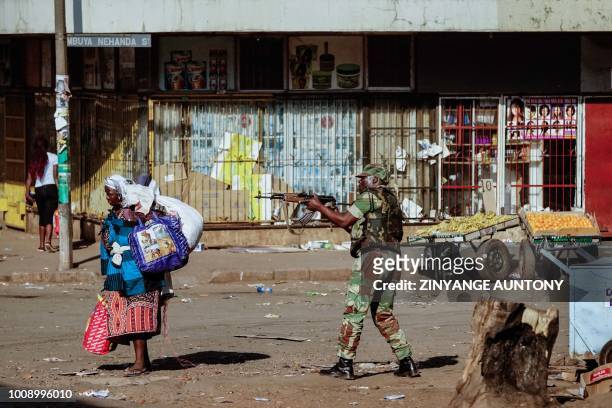 Vendor scurries for cover with her wares as soldiers disperse demonstrators on August 1 2018, in Harare, after protests erupted over alleged fraud in...