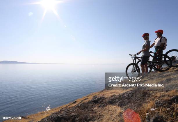 mountain biking couple pause on hillside above calm sea - vancouver island stock pictures, royalty-free photos & images