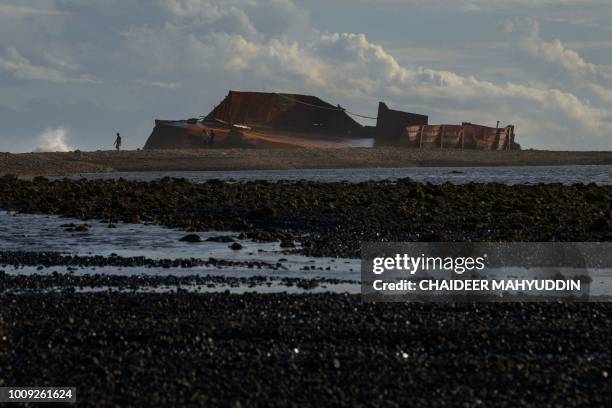 This photo taken on August 1, 2018 shows people walking along a coal-strewn beach after two barges transporting coal ran aground on Lhoknga beach in...