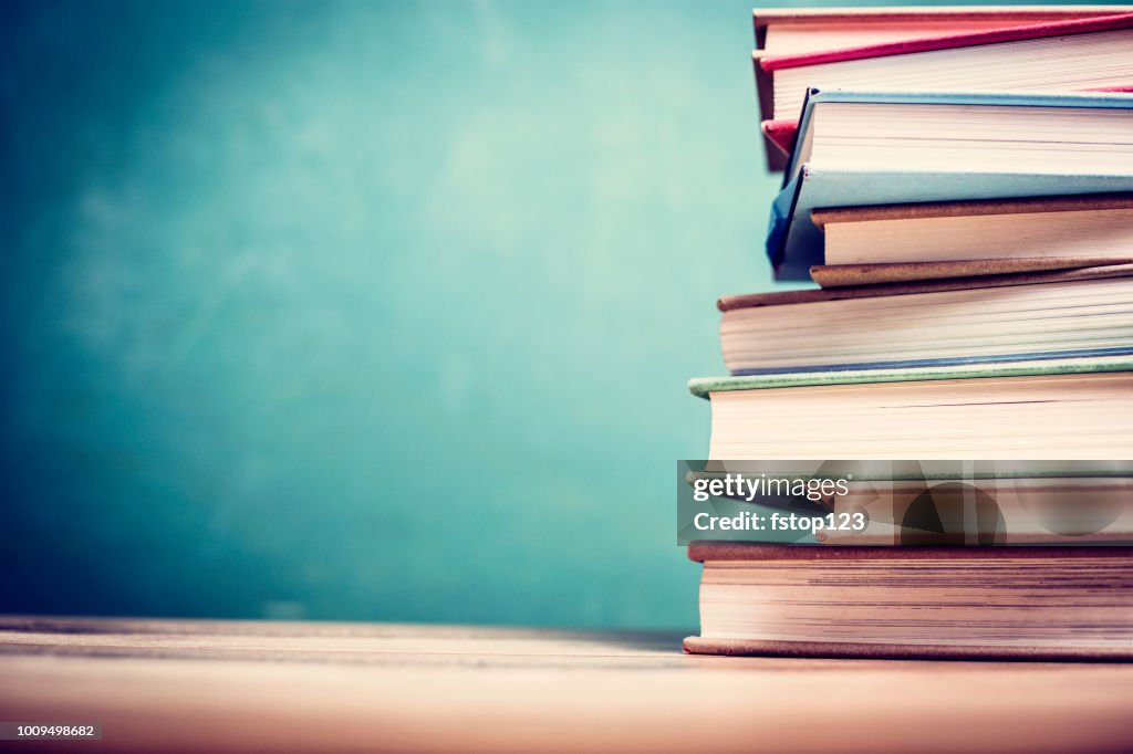 Textbooks on wooden school desk with chalkboard.
