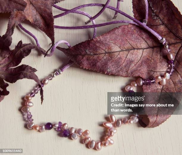a pearl and amethyst necklace with autumn leaves. still life. - pearl necklace stockfoto's en -beelden