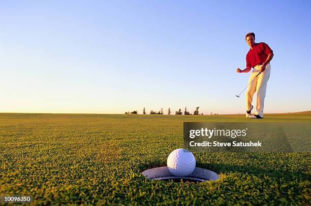 man golfer sinking putt on green - golfbal stockfoto's en -beelden