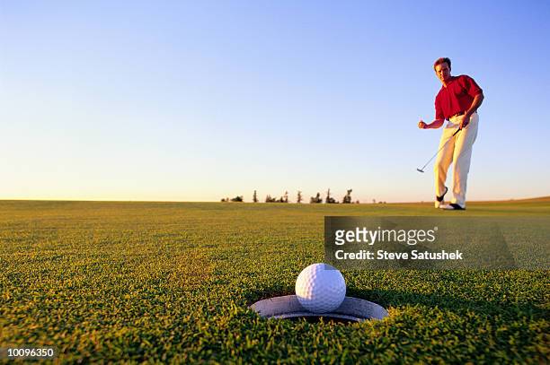 man golfer sinking putt on green - golfgreen stock pictures, royalty-free photos & images