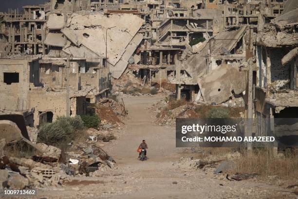 Picture taken on August 2 shows a man riding a motorcycle past destroyed buildings in the opposition-held southern city of Daraa.