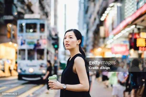beautiful young woman using smartphone in busy city street, against colourful neon commercial sign and city buildings - busy coffee shop stockfoto's en -beelden