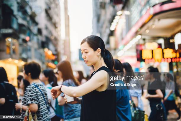 busy woman checking time on wristwatch while walking on pedestrian crossing in city, against a group of woman commuters - busy coffee shop stockfoto's en -beelden
