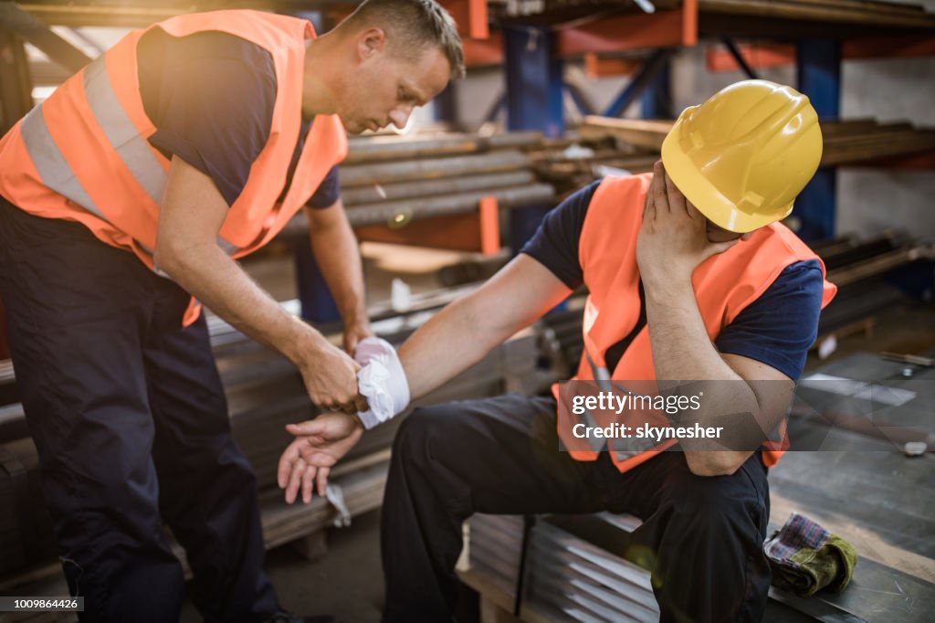 Trabajador manual que ayuda a su colega con lesiones físicas en el molino de acero.