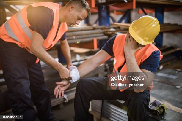 manual worker assisting his colleague with physical injury in steel mill. - work injury stock pictures, royalty-free photos & images