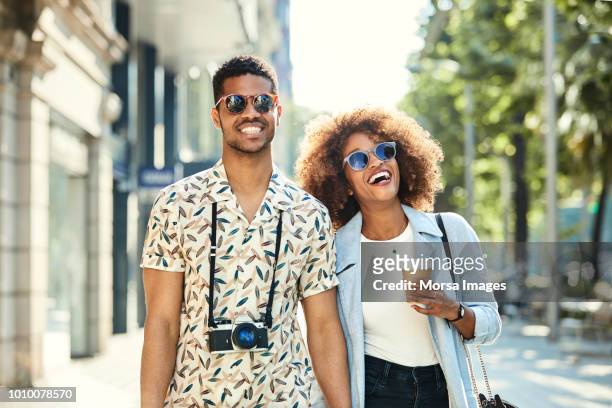 cheerful young couple walking on sidewalk in city - young couple exploring city stock pictures, royalty-free photos & images