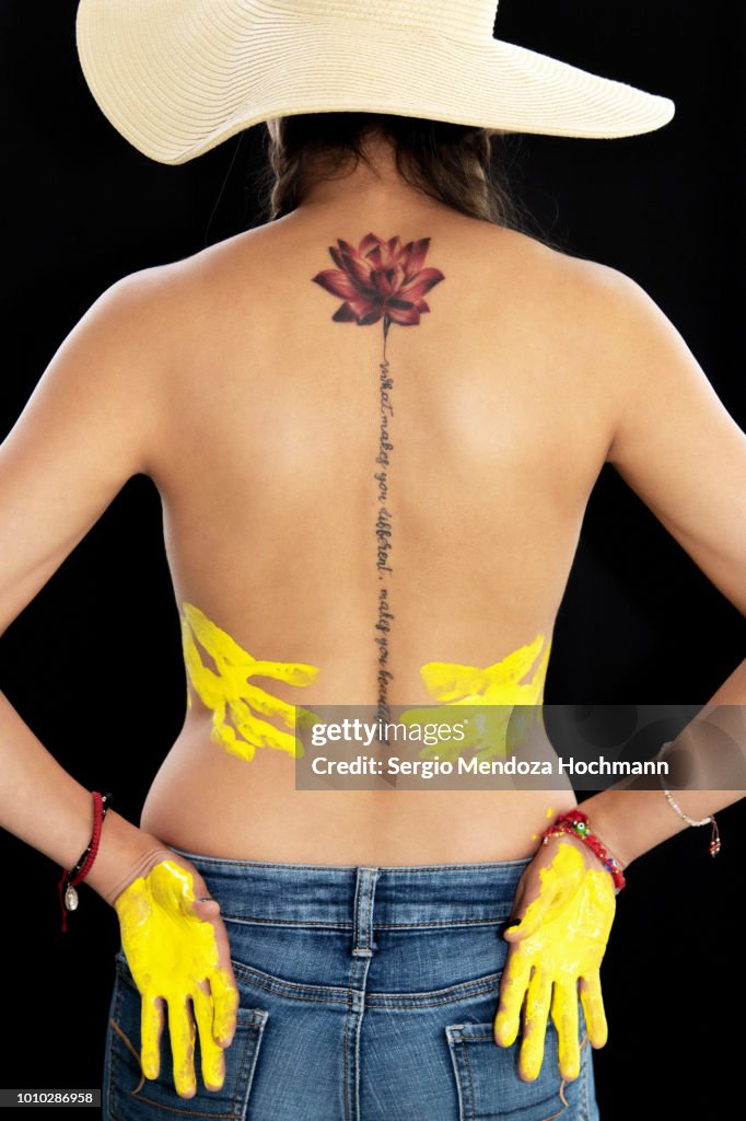 A young woman's back with a lotus flower tattoo and her hands with paint