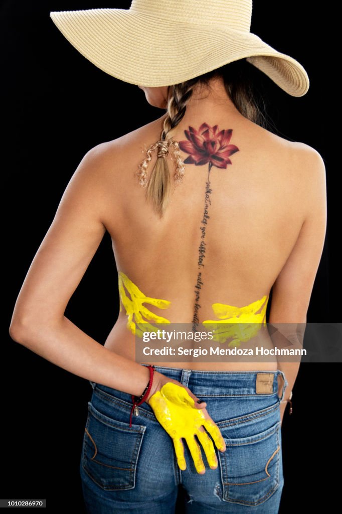 A young woman's back with a lotus flower tattoo and her hands with paint