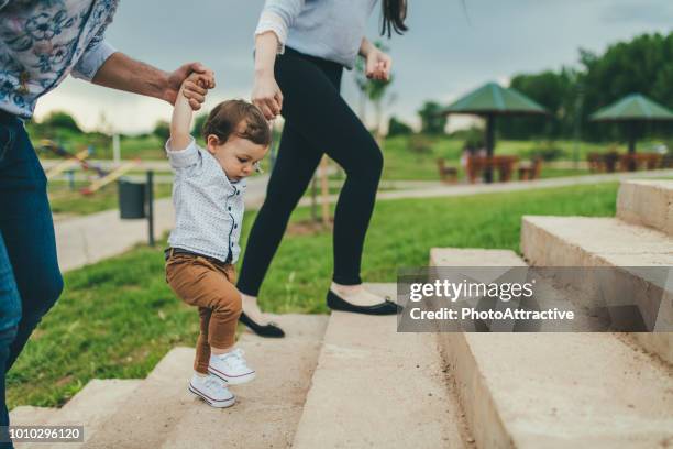 baby lopen met hulp van haar ouders - eerste stappen - stappen stockfoto's en -beelden