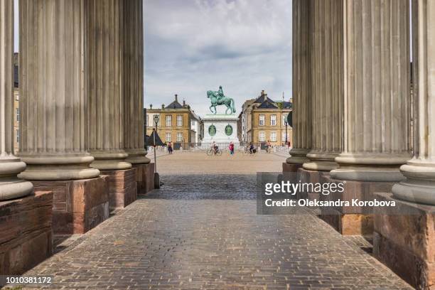 view of the amalienborg square and a statue of frederik v on horseback through a walkway framed with columns. - amalienborg palace stock pictures, royalty-free photos & images