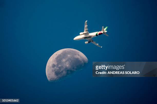 An Italian Alitalia aeroplane flies with the moon in the background over the sky of the capital Rome on August 3, 2018.