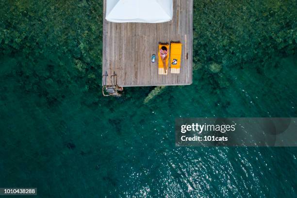 beautiful woman sunbathing alone on a wooden pier in sea aerial photo - beach bag overhead stock pictures, royalty-free photos & images