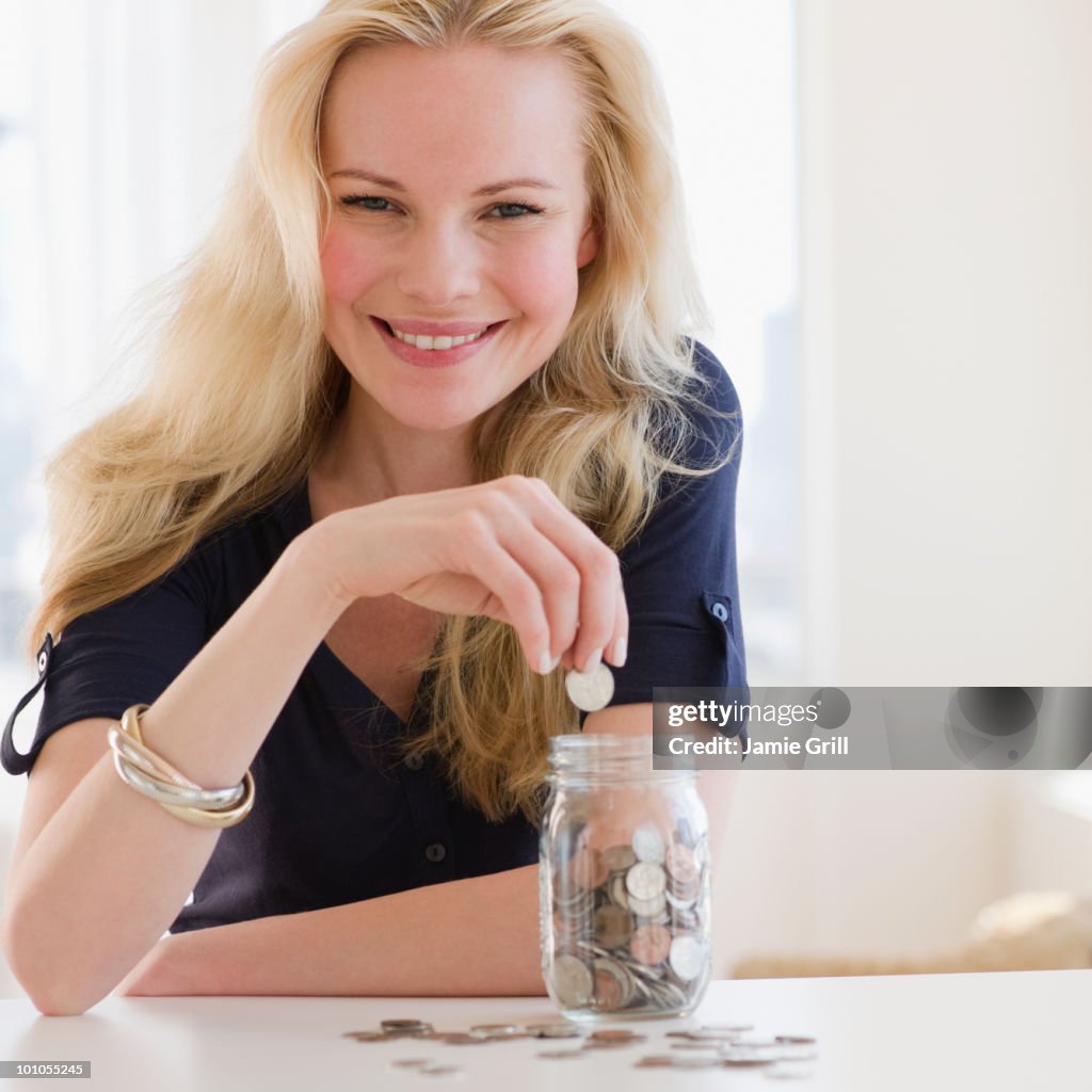 Young woman putting coin in jar of money