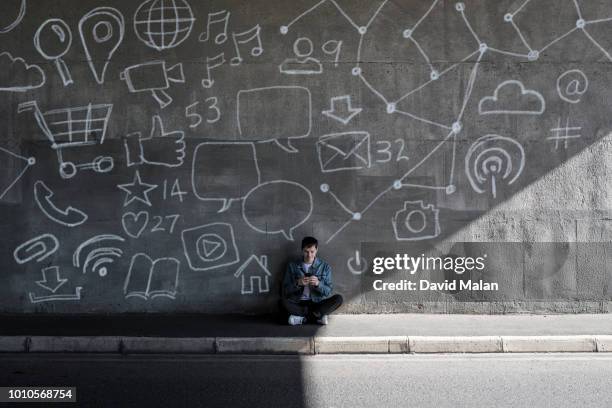 person using mobile device in front of a wall illustrated with tech symbols. - distraído imagens e fotografias de stock