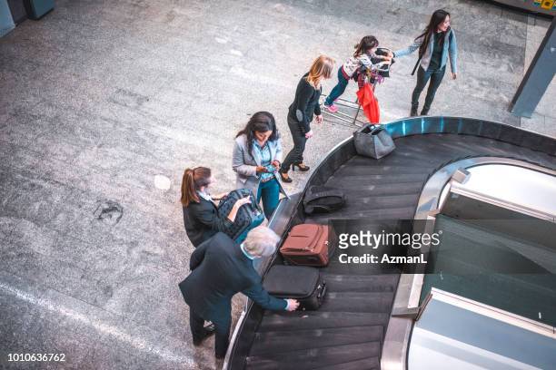 personas a la espera de equipaje en terminal del aeropuerto - zona de equipajes fotografías e imágenes de stock