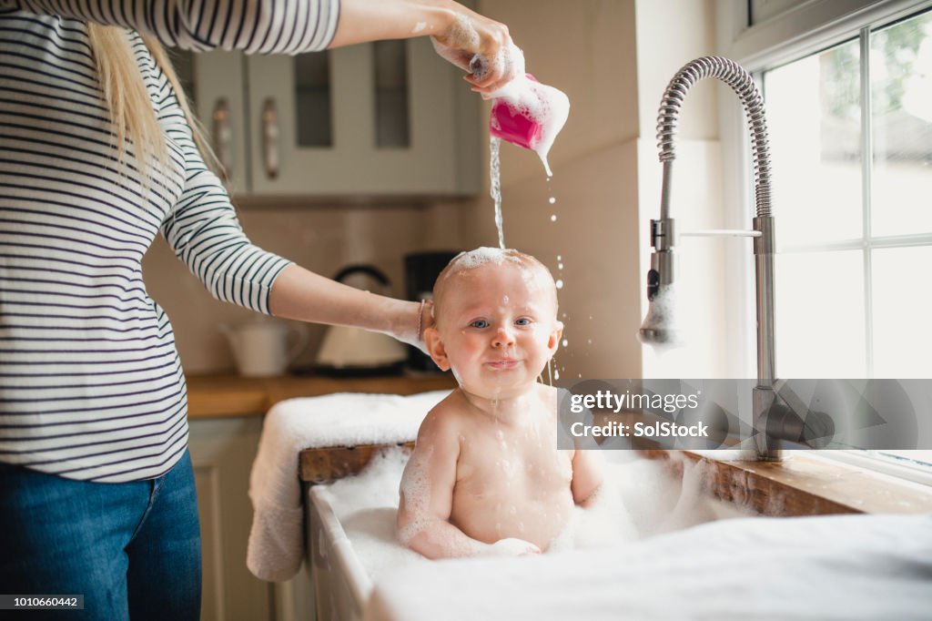 Mutter gießt Wasser über Babys Kopf