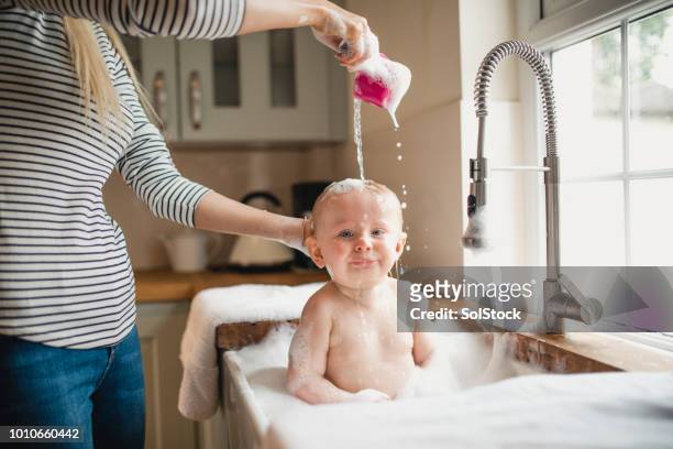 mor häller vatten över spädbarn huvud - bathtub bildbanksfoton och bilder