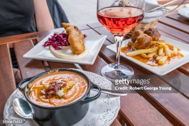 an outdoor table at a restaurant in triana. in the foreground salmorejo (gazpacho with crumbled ham and cheese), left rear is merluza frita machacada (battered fried hake), right rear boulette de maison (meatballs and french fries) & rosé. - terrasse maison stock-fotos und bilder