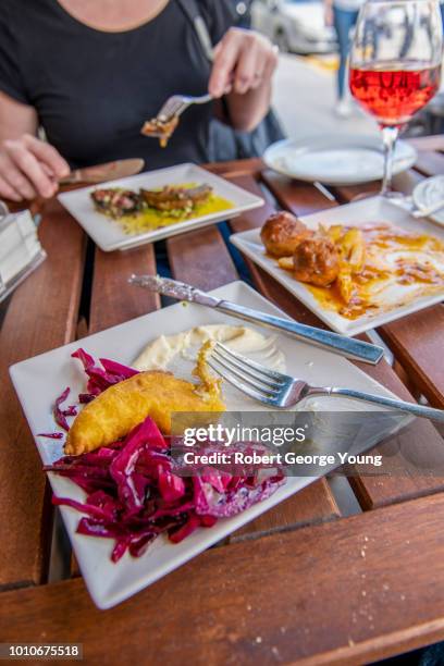 dining at an outdoor table at a restaurant in triana. in the foreground is merluza frita machacada (battered fried hake with pickled cabbage), left rear is tapa de seta con ajo y tomate (mushroom caps with garlic and tomato) and right are meatballs. - merluza stockfoto's en -beelden