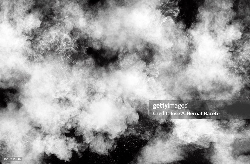 Full frame of forms and textures of an explosion of powder and smoke of color white on a black background.