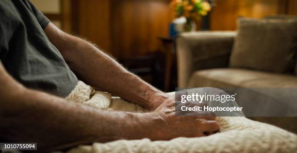 een oudere blanke man handen in zijn schoot bedekt zit alleen in een woonkamer - op schoot stockfoto's en -beelden