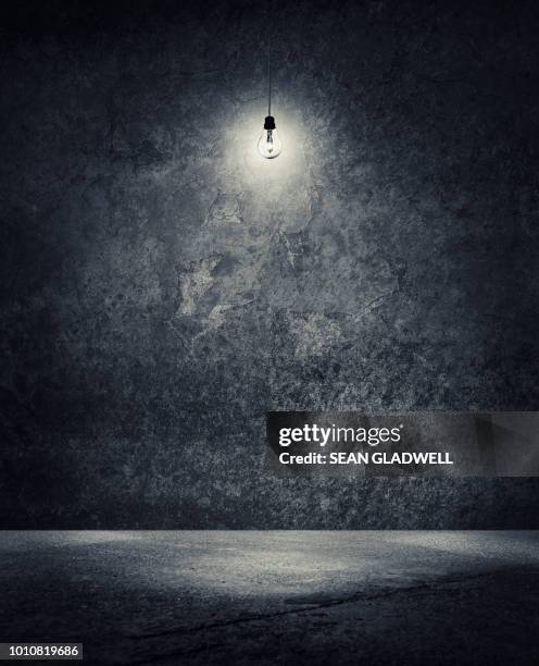 light bulb hanging from ceiling in empty space - dark room stock-fotos und bilder