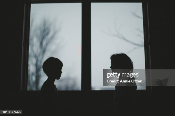 two children’s silhouettes in front of window - brother and sister silhouette stock pictures, royalty-free photos & images