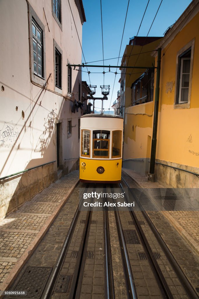 The Elevador da Bica yellow electric tram travels up the street at sunset.