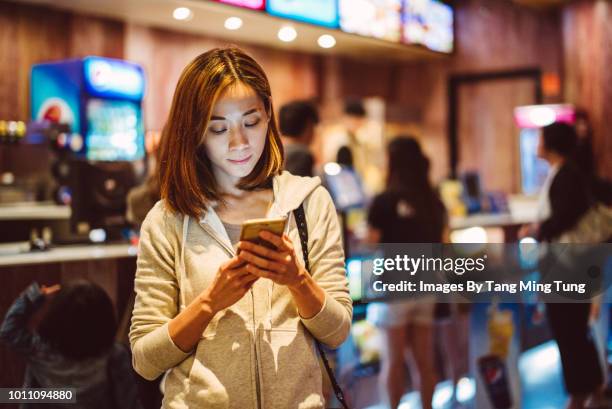 pretty young lady using smartphone in a cinema's box office / concession stand. - kinokasse stock-fotos und bilder