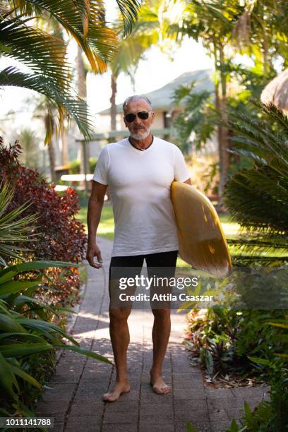 portrait of smiling senior man with surfboard by palmtrees - sunshine coast australia stock pictures, royalty-free photos & images