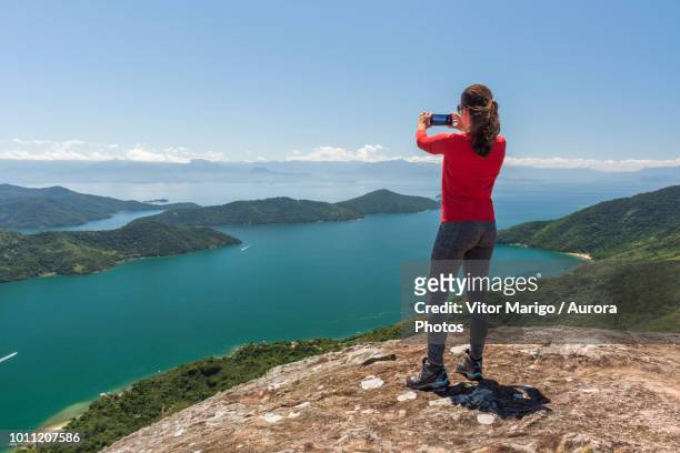 woman photographing view of sea from mountain, saco do mamangua, paraty, costa verde, brazil - femme de dos smartphone photos et images de collection