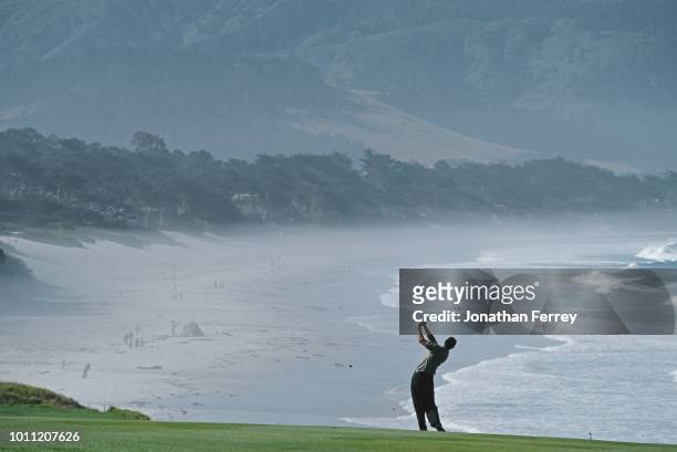 Tiger Woods of the United States silhouetted against the oceanside backdrop as he plays from the ninth fairway during the the 100th United States...