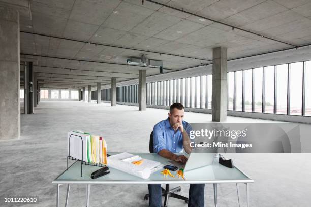 a caucasian male business owner at his temporary desk in a new raw business space. - empty office one person stock pictures, royalty-free photos & images